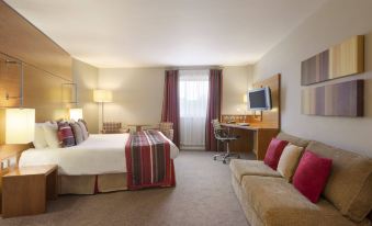 a hotel room with a king - sized bed , a couch , and a tv . also a dining table in the room at Ramada Plaza by Wyndham Wrexham