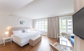 a modern bedroom with two beds , a desk , and large windows , all situated in a spacious living area at NH Geneva City