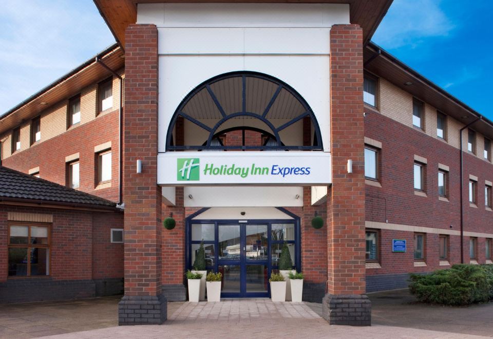 a brick building with a holiday inn express sign on the front , surrounded by greenery at Holiday Inn Express Warwick - Stratford-Upon-Avon