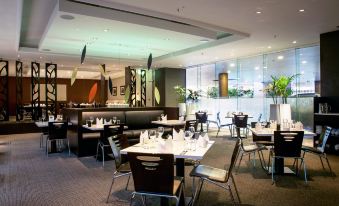 a modern restaurant with various dining tables and chairs , as well as a bar area at Grand Millennium Auckland