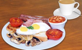 a plate of breakfast food , including eggs , bacon , sausage , mushrooms , and tomatoes , accompanied by a cup of coffee at Mandarin Motel