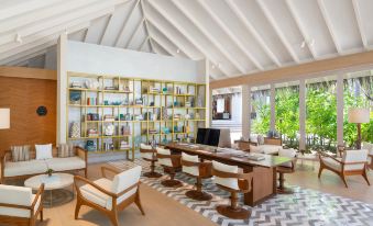 a modern living room with a large bookshelf filled with books , wooden chairs and tables , and a tv mounted on the wall at JW Marriott Maldives Resort & Spa