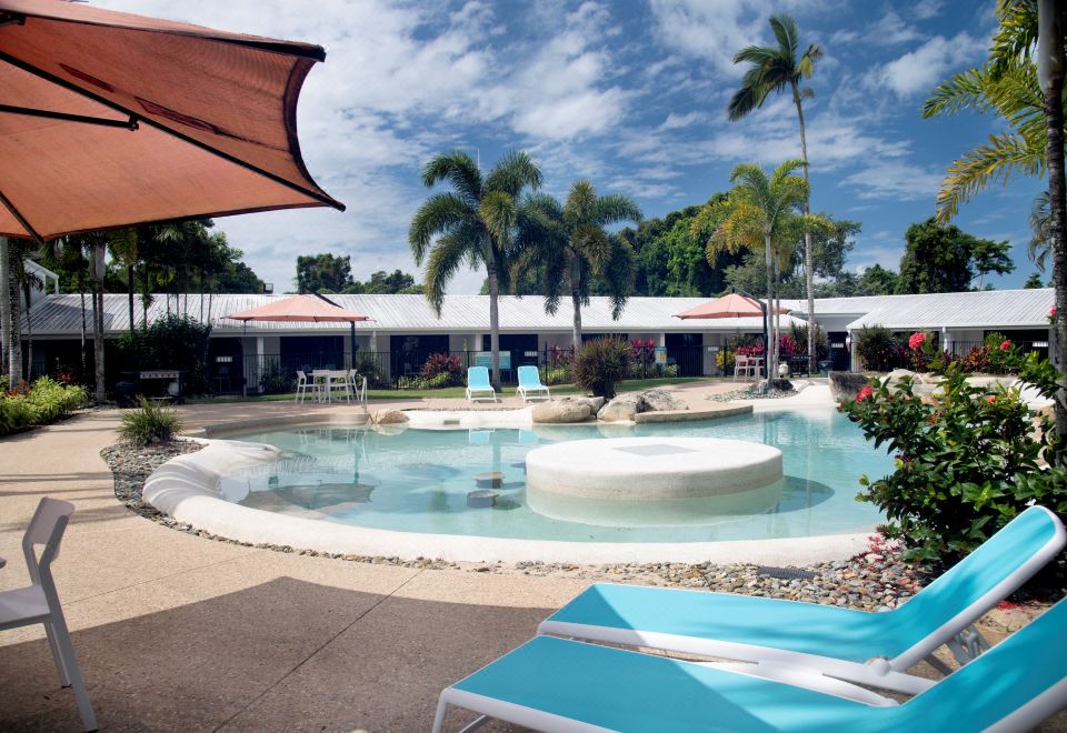 a large outdoor pool surrounded by lounge chairs and umbrellas , with palm trees in the background at Mission Beach Resort