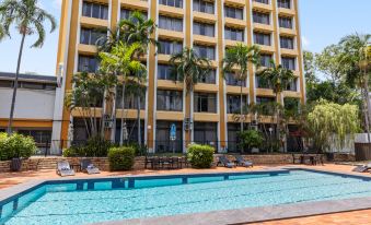 a large hotel with a swimming pool surrounded by palm trees , chairs , and umbrellas , providing a relaxing atmosphere at Frontier Hotel Darwin