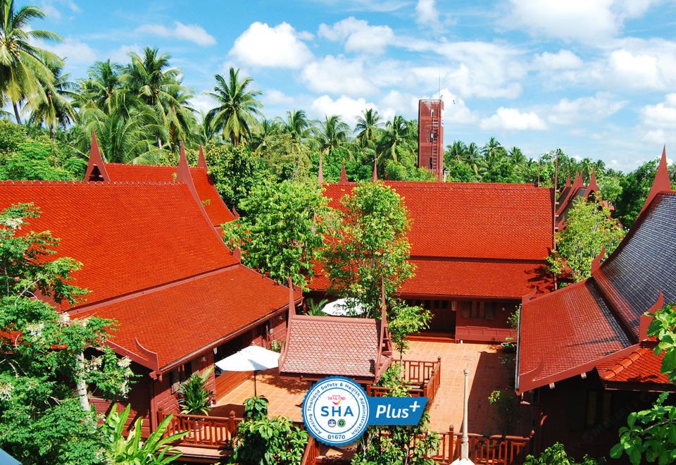 a large red building with a tall tower is surrounded by palm trees and tropical plants at Baan Amphawa Resort & Spa