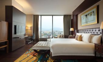 a large bed with white linens is in a room with a colorful rug and a view of the city at Hilton Bandung