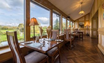 a restaurant with wooden tables and chairs , set for dining , has large windows overlooking the outdoors at Damson Dene Hotel