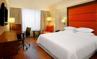 a large bed with white linens is in a room with wooden floors and orange accents at Four Points by Sheraton Ahmedabad