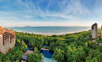 The aerial view displays a beach, ocean, and a resort featuring swimming pools on either side at Pullman Oceanview Sanya Bay Resort & Spa
