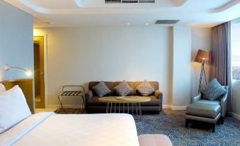 a modern hotel room with a bed , couch , and chair , along with a table and lamp at Hotel Ciputra Cibubur Managed by Swiss-Belhotel International