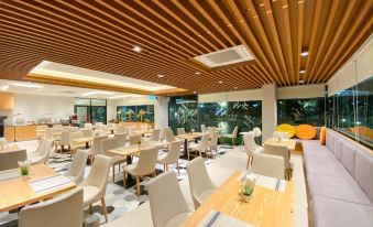 a modern restaurant with wooden tables and chairs , white cushions on the tables , and large windows at Hotel Fuse Rayong