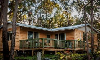 a wooden cabin with a green railing and a covered porch is surrounded by trees at Balingup Heights Hilltop Forest Cottages