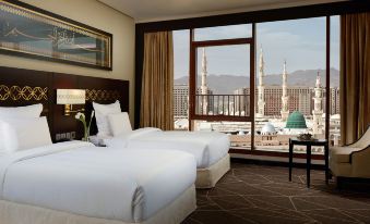 a hotel room with two beds , a desk , and a window overlooking a cityscape outside at Pullman Zamzam Madina