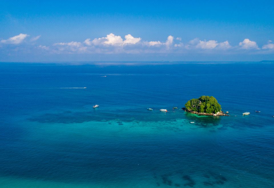 an aerial view of a small island surrounded by clear blue water , with boats in the distance at Berjaya Tioman Resort