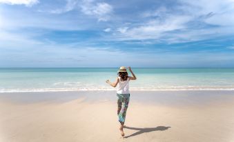 a woman wearing a hat is walking on a sandy beach , enjoying the sun and the ocean at Grand Mercure Khao Lak Bangsak