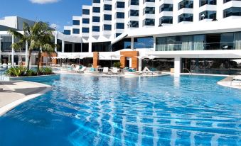 a large outdoor swimming pool surrounded by a hotel , with people enjoying their time in the pool at Crown Metropol Perth