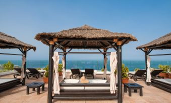 a beach scene with a group of people sitting under a thatched roof on a sunny day at Landmar Costa Los Gigantes