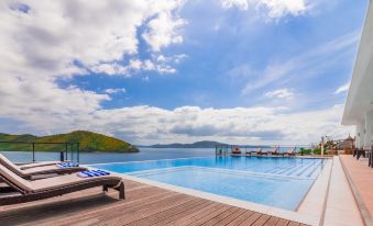 a large outdoor swimming pool surrounded by grass and trees , with a wooden deck extending from the side at Busuanga Bay Lodge