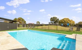 a large swimming pool surrounded by a grassy field , with trees in the background and a fence surrounding the pool at The Wine Vine Hotel