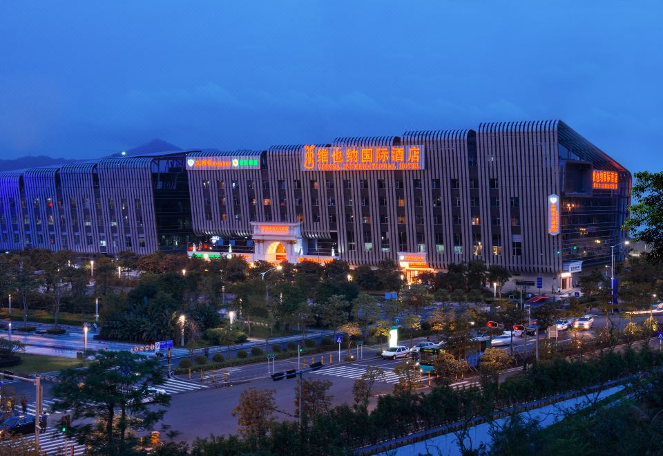 In the middle of an urban area, there is a large building with many windows that is illuminated at night at Vienna International Hotel (Shenzhen North Railway Station)