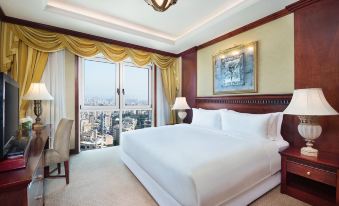 a large , well - lit hotel room with a white bed and a view of the city through a window at Hilton Beirut Metropolitan Palace