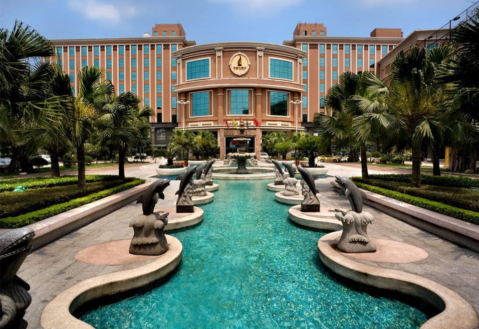 a large building with a fountain in front of it , surrounded by palm trees and statues at City Hotel