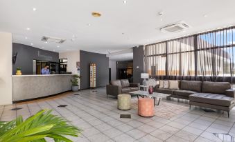 a spacious , well - lit hotel lobby with various seating arrangements and a reception desk , featuring a large window and couches at Frontier Hotel Darwin