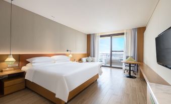 The bedroom features a double bed, a large window, and a balcony with a beachfront view at Vienna International Hotel (Baoting Center)