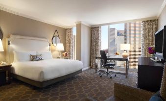 a large , well - lit hotel room with a white bed , a desk , and a window overlooking the city at Fairmont Dallas
