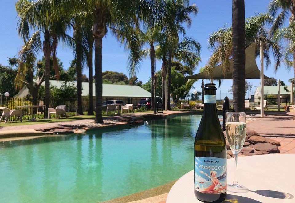 a bottle of wine and a glass are placed on a table near a pool , with palm trees in the background at Murray Downs Resort