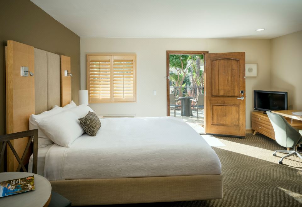 a large , well - made bed is in a bedroom with a wooden door and windows leading to an outdoor area at Catalina Canyon Inn