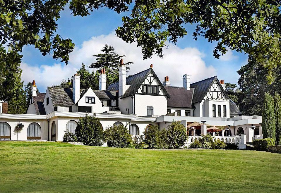 a large white mansion with a red roof sits on a green lawn surrounded by trees at Hilton Cobham