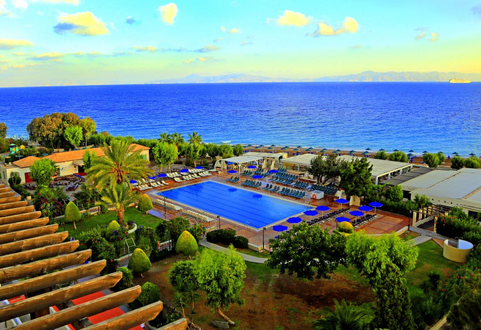 a resort with a large pool surrounded by palm trees and lush greenery , overlooking the ocean at Labranda Blue Bay Resort