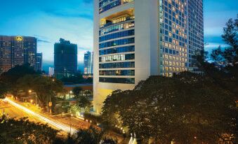 a modern office building lit up at night , surrounded by trees and a busy city street at Hotel Maya Kuala Lumpur City Centre