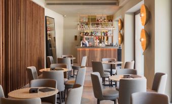 a modern dining room with wooden tables and chairs , a bar area , and a bar counter at H10 Palacio Colomera