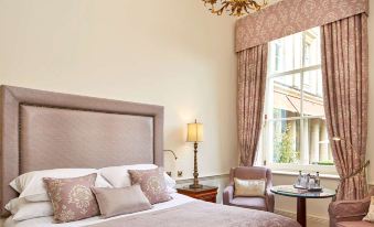 a large bed with a pink blanket is in a room with a chandelier and chairs at Macdonald Bath Spa Hotel