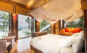 a luxurious bedroom with a canopy bed , large windows , and a view of the ocean at Soneva Kiri