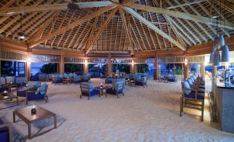 a large , open room with a thatched roof and thatched ceiling , surrounded by wooden furniture and surrounded by sand at Mirihi Island Resort