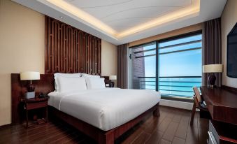 The bedroom features large ocean-view windows and a balcony, with an elegant bed at Pullman Oceanview Sanya Bay Resort & Spa