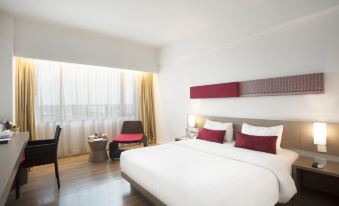 a modern hotel room with white walls , wooden floors , and a large bed with red pillows at Grand Zuri Dumai