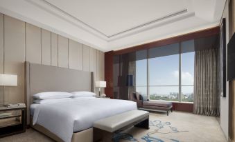 The bedroom features large windows and a balcony that offer a city view, along with an elegant bed positioned in the front at the International Trade City, Yiwu - Marriott Executive Apartments