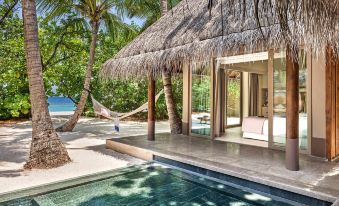 a luxurious villa with a thatched roof , a pool , and a hammock under the shade of palm trees at Joali Maldives