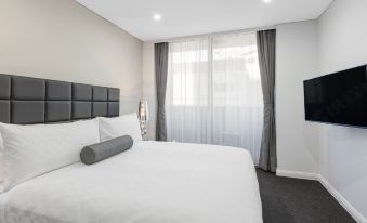 a modern bedroom with a white bed , grey curtains , and a flat - screen tv mounted on the wall at Meriton Suites North Sydney