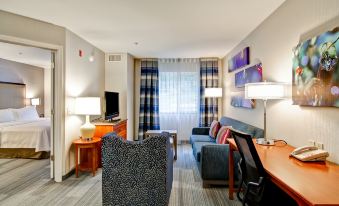 a modern hotel room with a living area featuring blue couches , wooden furniture , and large windows at Homewood Suites by Hilton Stratford