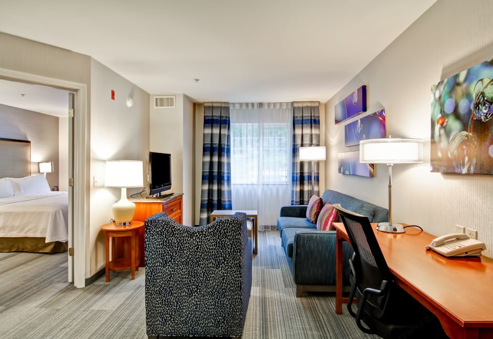 a modern hotel room with a comfortable couch , desk , and dining area , all decorated in shades of blue and green at Homewood Suites by Hilton Stratford