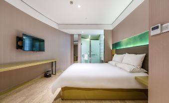 A modern bedroom features a large bed and a flat-screen TV positioned in the center on an elevated surface at Hanting Youjia Hotel (Shanghai East Nanjing Road Branch)