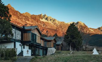 a group of wooden houses surrounded by a grassy field , with mountains in the background at The Rock Hotel