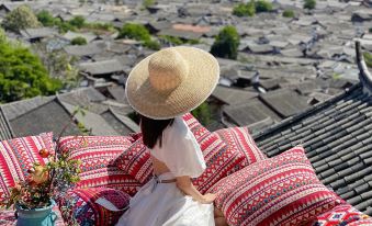 A woman sits on the floor with pillows and blankets, looking out at the view from her room at Lijiang YueJiaren · White Horse Luxury Homestay