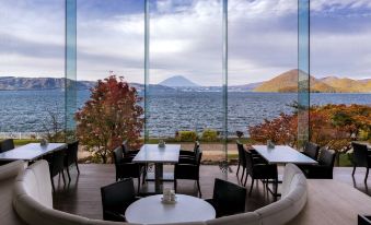 a dining area with a view of a lake , surrounded by glass walls and tables at The Lake View Toya Nonokaze Resort