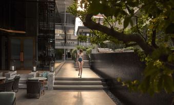 A woman walks through the courtyard with her back to the camera, while another person is sitting nearby at HOMM Sukhumvit34 Bangkok - a brand of Banyan Group